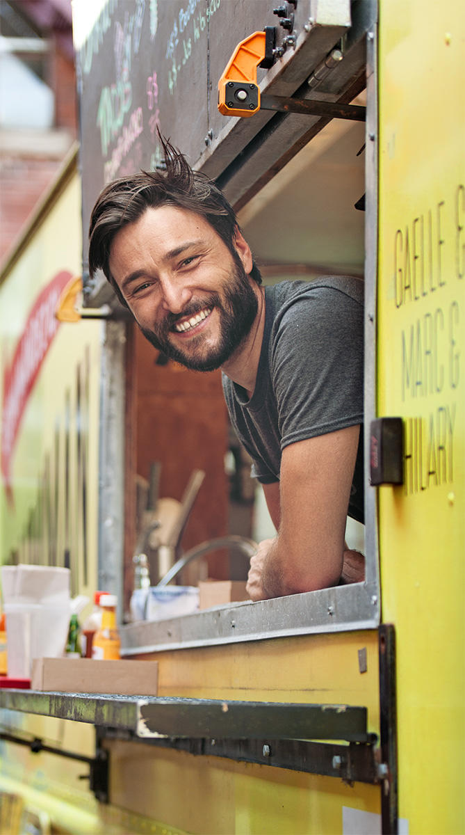 A smiling man leans out of the window of a brightly painted food truck